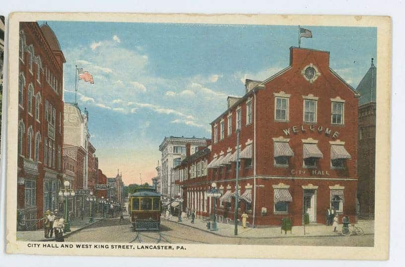 An old photo of a trolly going through a city.