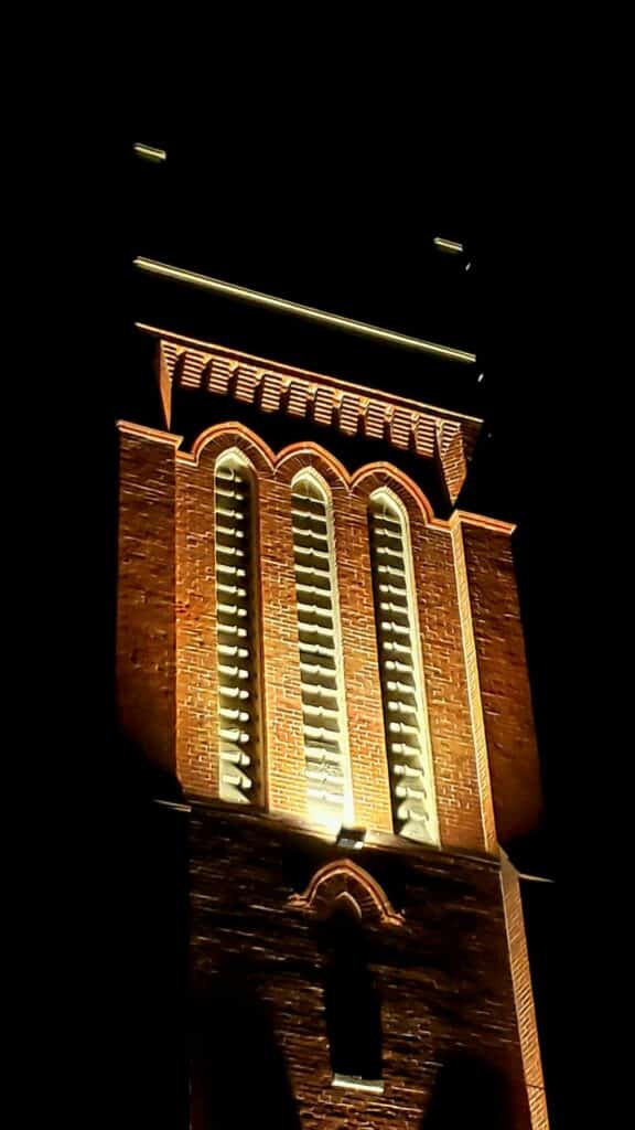 A large, historic, brick tower lit up at night.