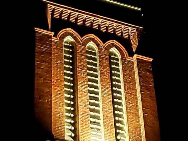 A large, historic, brick tower lit up at night.
